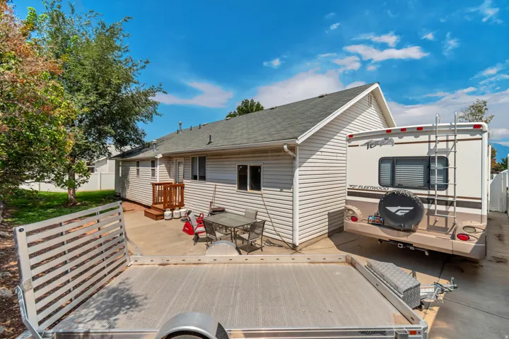 Spacious outdoor living area featuring a composite deck with integrated seating spaces, vinyl fencing, mature landscaping, and RV parking
