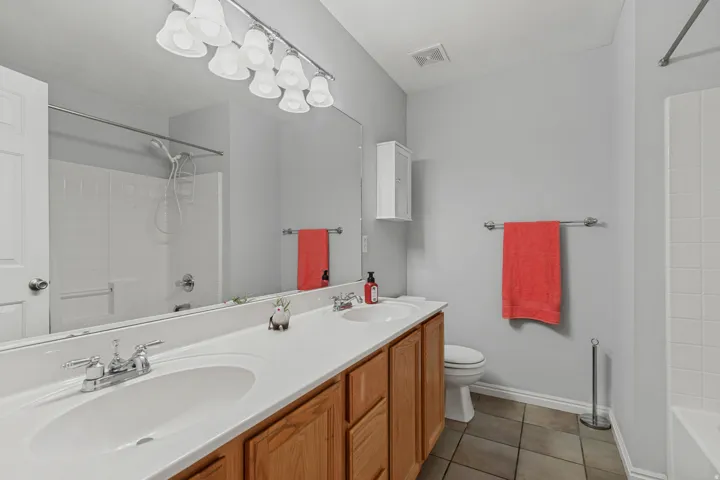 Double vanity with wood-finish cabinetry, white countertop, chrome fixtures, and a large wall mirror