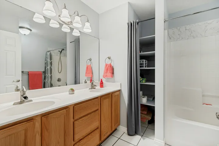 Dual basin vanity with wood-finish cabinetry, built-in shelving, and a tiled shower-over-tub combination