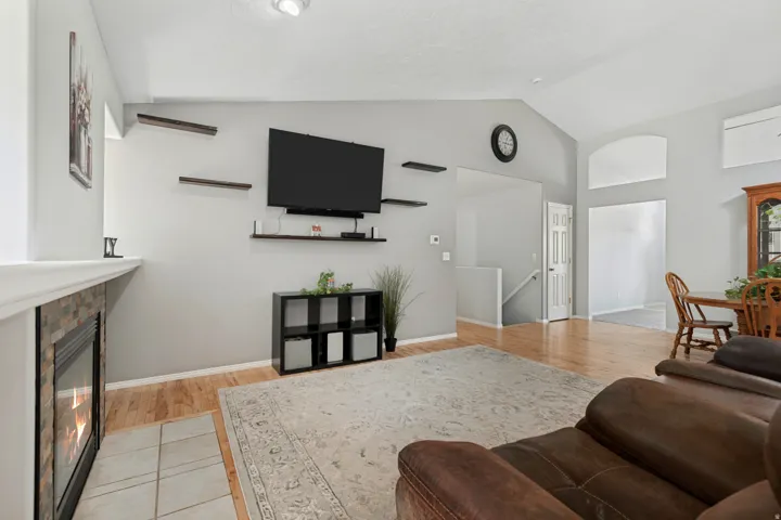 Living area with vaulted ceiling, fireplace featuring stone tile surround, hard-surface flooring, and an archway
