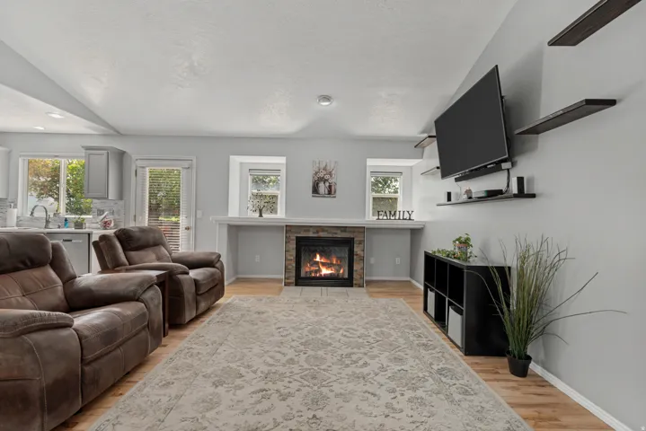 Vaulted ceiling living space with wood-finish flooring, a stone-faced fireplace, and built-in shelving