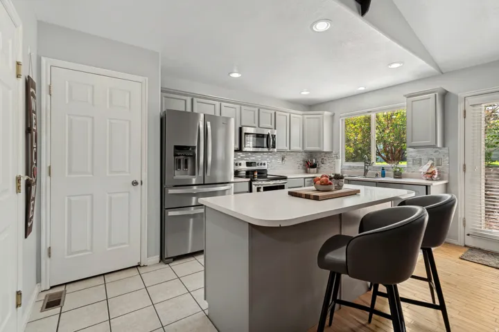 Kitchen featuring light gray cabinetry, stainless steel appliances, a center island with countertop seating, a tiled backsplash, and recessed lighting