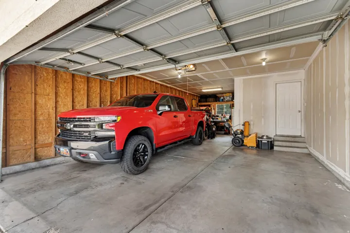 Attached garage with concrete flooring, exposed wood paneling, and an interior access door