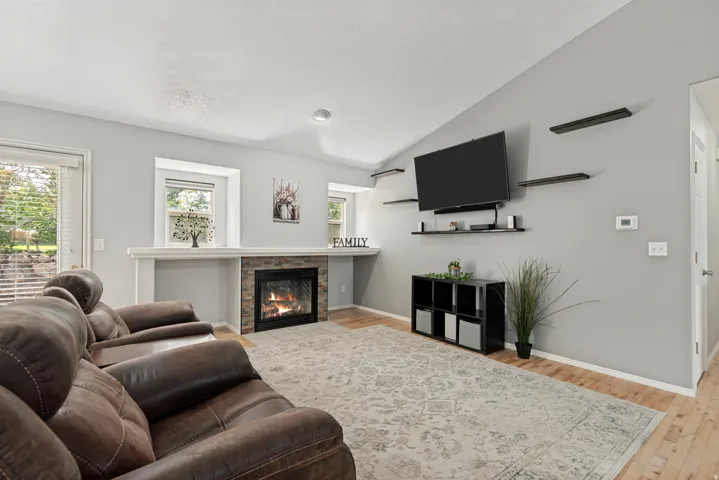 Vaulted ceiling accentuates this living area featuring a stone-faced fireplace with a white mantel, and wood-finish flooring