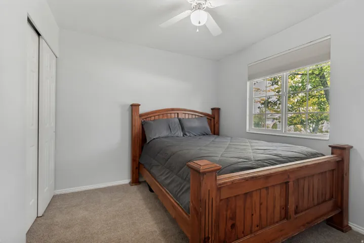 Carpeted room featuring a ceiling fan, a window with roller shade, and bi-fold closet doors