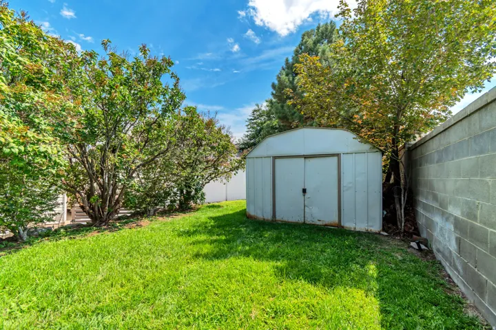 Expansive backyard featuring a manicured lawn, established trees, privacy fencing, and a storage shed