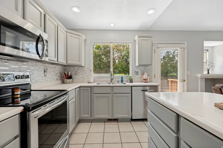 Gray shaker-style cabinetry with stainless steel appliances, tiled backsplash, recessed lighting, and a white countertop