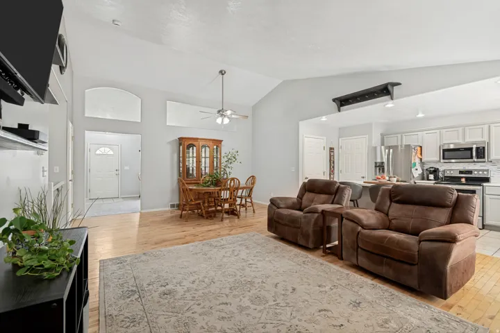 Vaulted ceiling with ceiling fan, wood-finish flooring, white kitchen cabinetry, stainless steel kitchen appliances, and recessed lighting