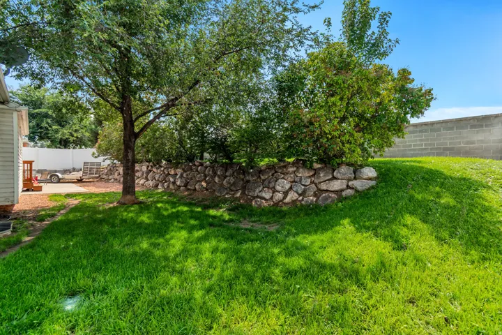 Expansive backyard featuring a manicured lawn, mature trees, and a stone retaining wall