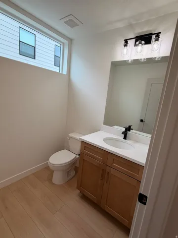 Powder room featuring wood-finish flooring, a contemporary vanity with a white countertop and integrated sink, a dark-finish faucet, and a modern three-light fixture