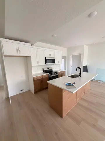 Kitchen featuring white upper cabinetry, wood-finish lower cabinetry, a center island with a sink, stainless steel appliances, and wood-finish LVP flooring