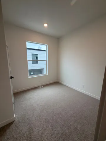 Recessed ceiling lighting, neutral carpet, white walls, and a large window