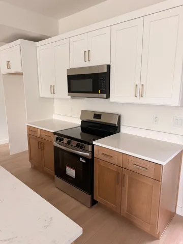 Two-tone cabinetry with white upper and wood-finish lower cabinets, stainless steel appliances, light-toned countertops, and wood-finish LVP flooring