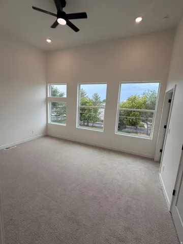 Primary bedroom. High ceilings with recessed lighting, black ceiling fan, multiple large windows, and neutral carpet flooring