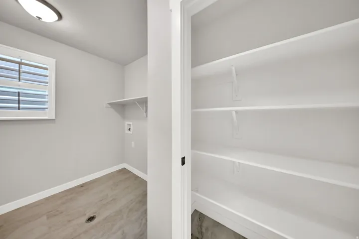 Laundry area with wood-finish flooring, a window with horizontal blinds, and a built-in shelf