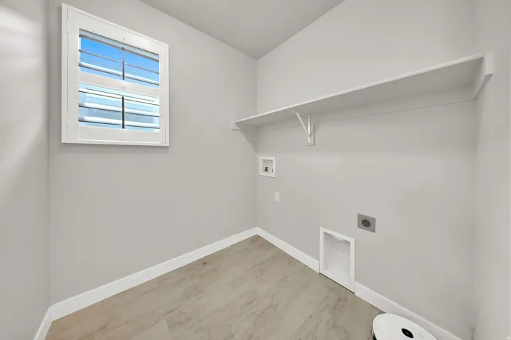 Laundry area featuring a window with white shutters, a built-in shelf, wall connections for washer and dryer, and light wood-finish flooring