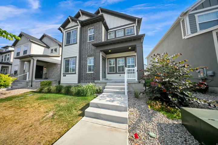Modern two-story residence featuring a charcoal brick and fiber cement exterior with peaked gable roofline, multi-pane windows, and a covered front entry with white railings