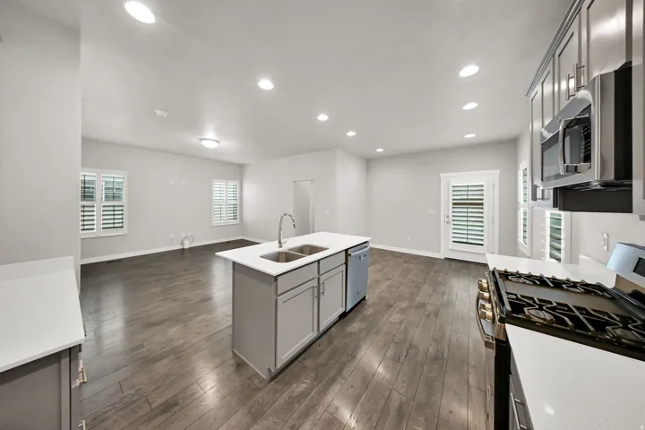 Kitchen island with double basin sink, stainless steel appliances, wood-finish flooring, recessed lighting, and white plantation shutters