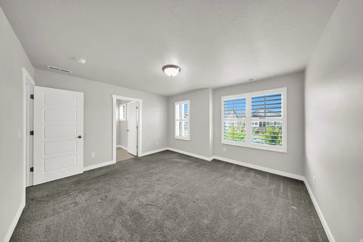 Primary Bedroom Spacious room featuring gray carpeting, light gray walls, white trim, and multiple windows with white plantation shutters