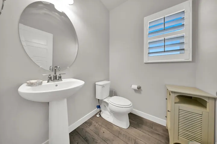 Half Bath, Pedestal sink with chrome-finish faucet, oval wall mirror, and wood-finish flooring