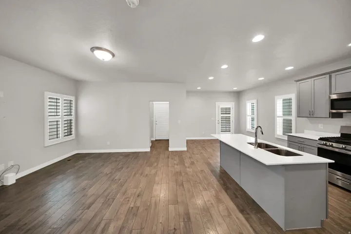 Open-concept living space with wood-finish flooring, white plantation shutters, recessed lighting, and a kitchen island with an undermount double sink