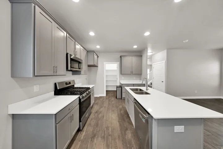 Modern kitchen featuring gray cabinetry, stainless steel appliances, a gas range, white countertops, and wood-finish flooring
