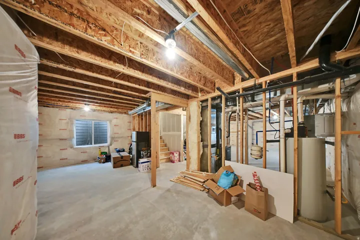Unfinished basement featuring exposed wood framing, concrete flooring, and a visible egress window