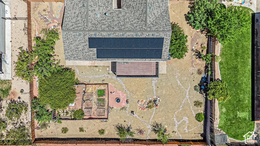 Roof with solar panels, ground-level deck, fenced backyard, raised garden beds, and rock pathways