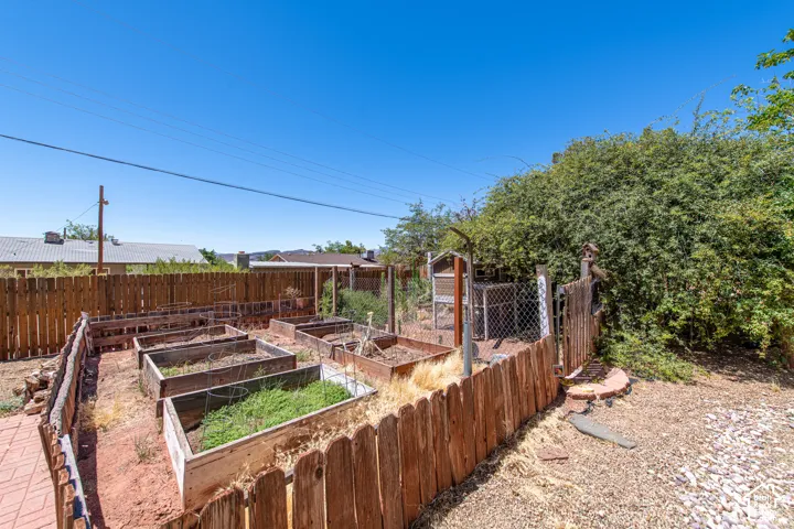 Multiple raised garden beds, wood fence perimeter, and a brick paver pathway