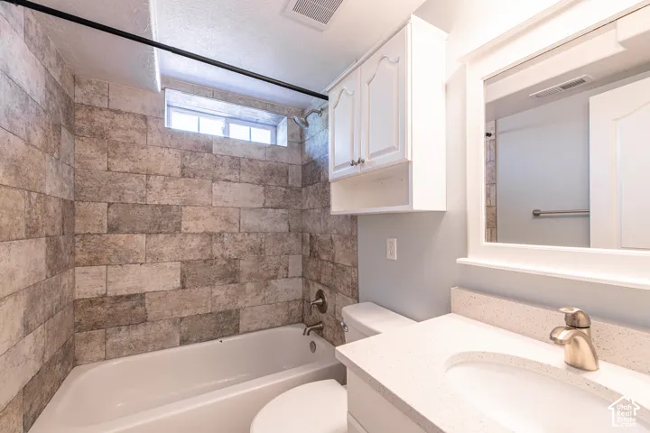 Bathroom featuring a tiled shower surround, built-in bathtub, and a vanity with an integrated sink and light-colored countertop