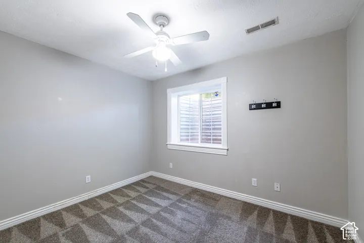 Light gray wall paint, patterned carpet flooring, white trim, ceiling fan with integrated lighting, and a white-framed window with blinds