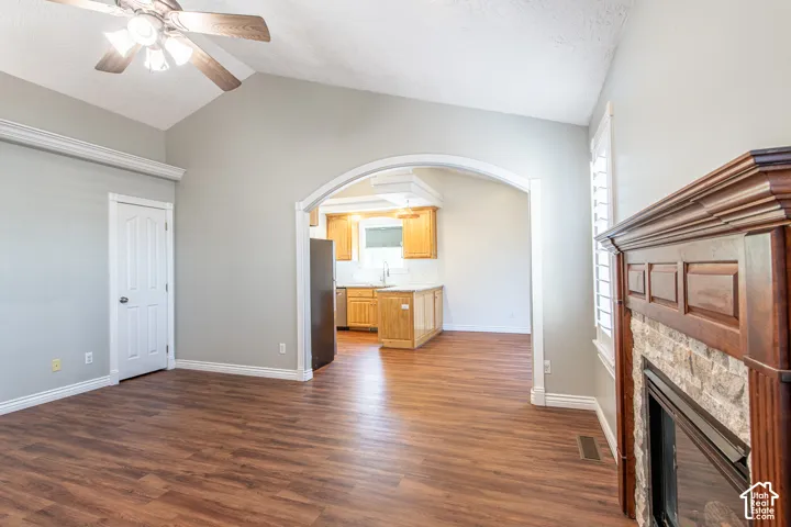 Vaulted ceiling with a ceiling fan, wood-finish flooring, stone-faced fireplace with wood mantel, and an arched entryway