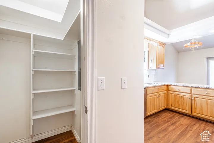 Built-in shelving, wood-finish flooring, light wood cabinetry, stone-finish countertops, and a tile backsplash
