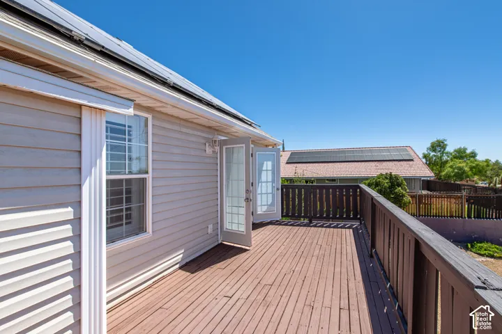 Expansive wood-finish deck with dark wood railing, double French doors, and vinyl siding