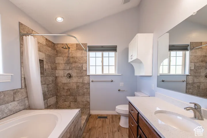 Bathroom featuring a built-in tub, tiled shower surround, recessed lighting, wood-finish flooring, and a vanity with an integrated sink and mirror