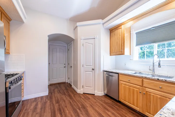 Kitchen featuring wood-finish flooring, light wood cabinetry, stainless steel appliances, granite countertops, and a subway tile backsplash