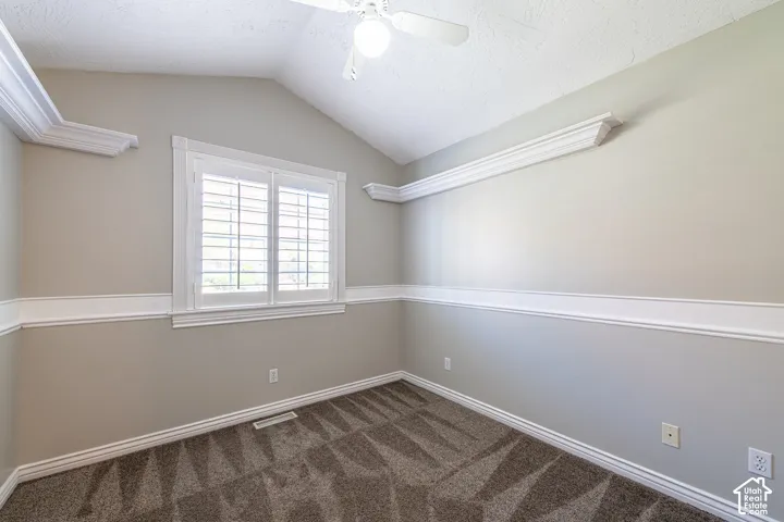 Vaulted ceiling with a ceiling fan, plantation shutters, crown molding, and wainscoting