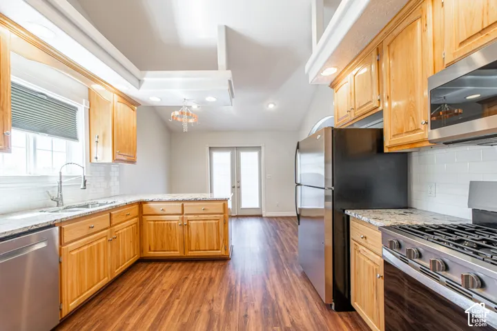 Wood-finish flooring, light wood cabinetry, white subway tile backsplash, light-toned countertops, and stainless steel appliances