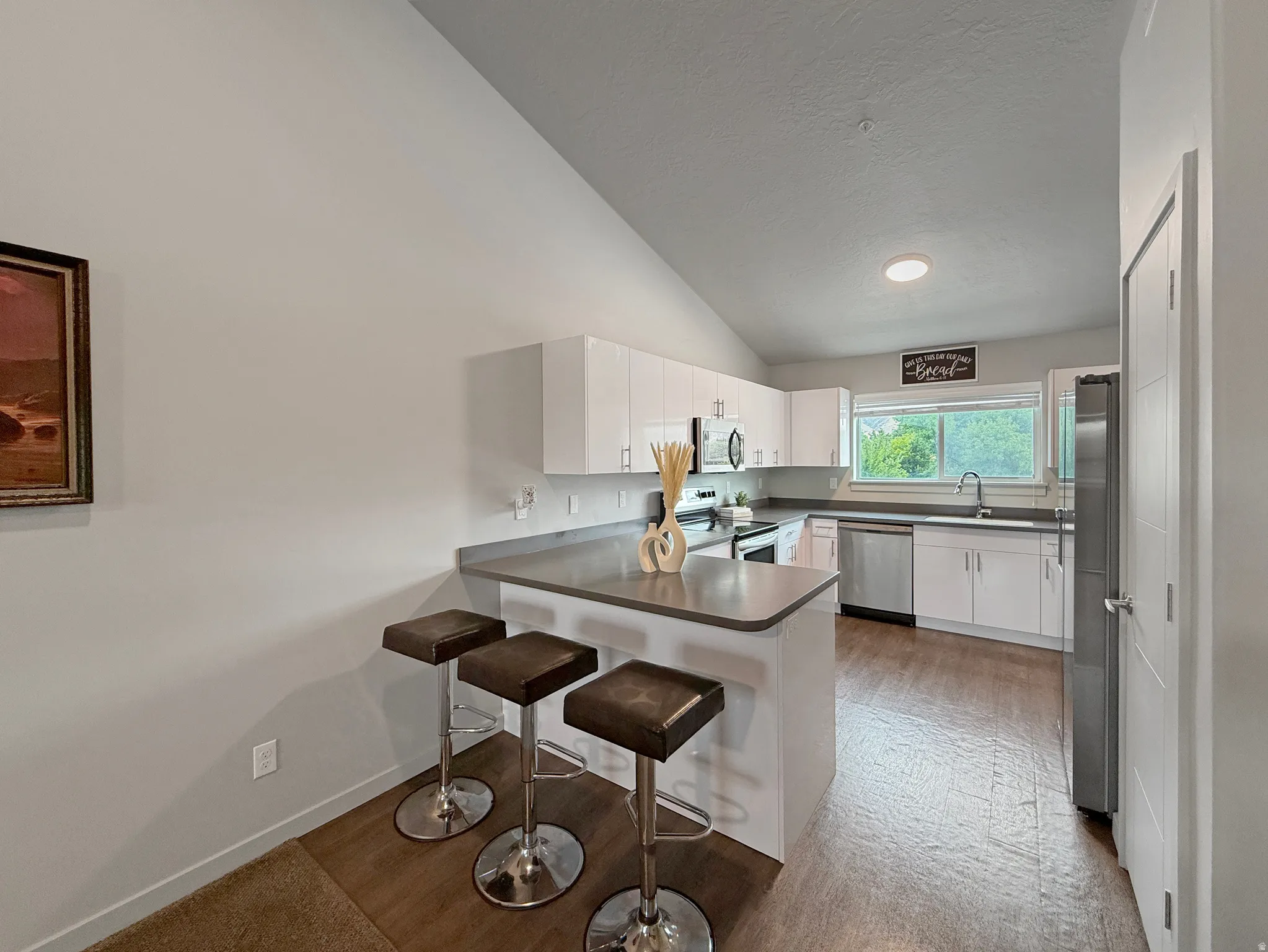 Kitchen featuring white cabinetry, stainless steel appliances, wood-finish flooring, and a breakfast bar with a solid surface countertop