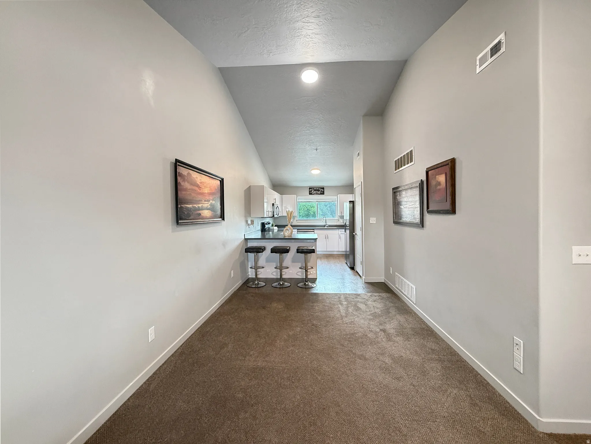 Vaulted ceiling, recessed lighting, carpet flooring, L-shaped kitchen counter, kitchen window