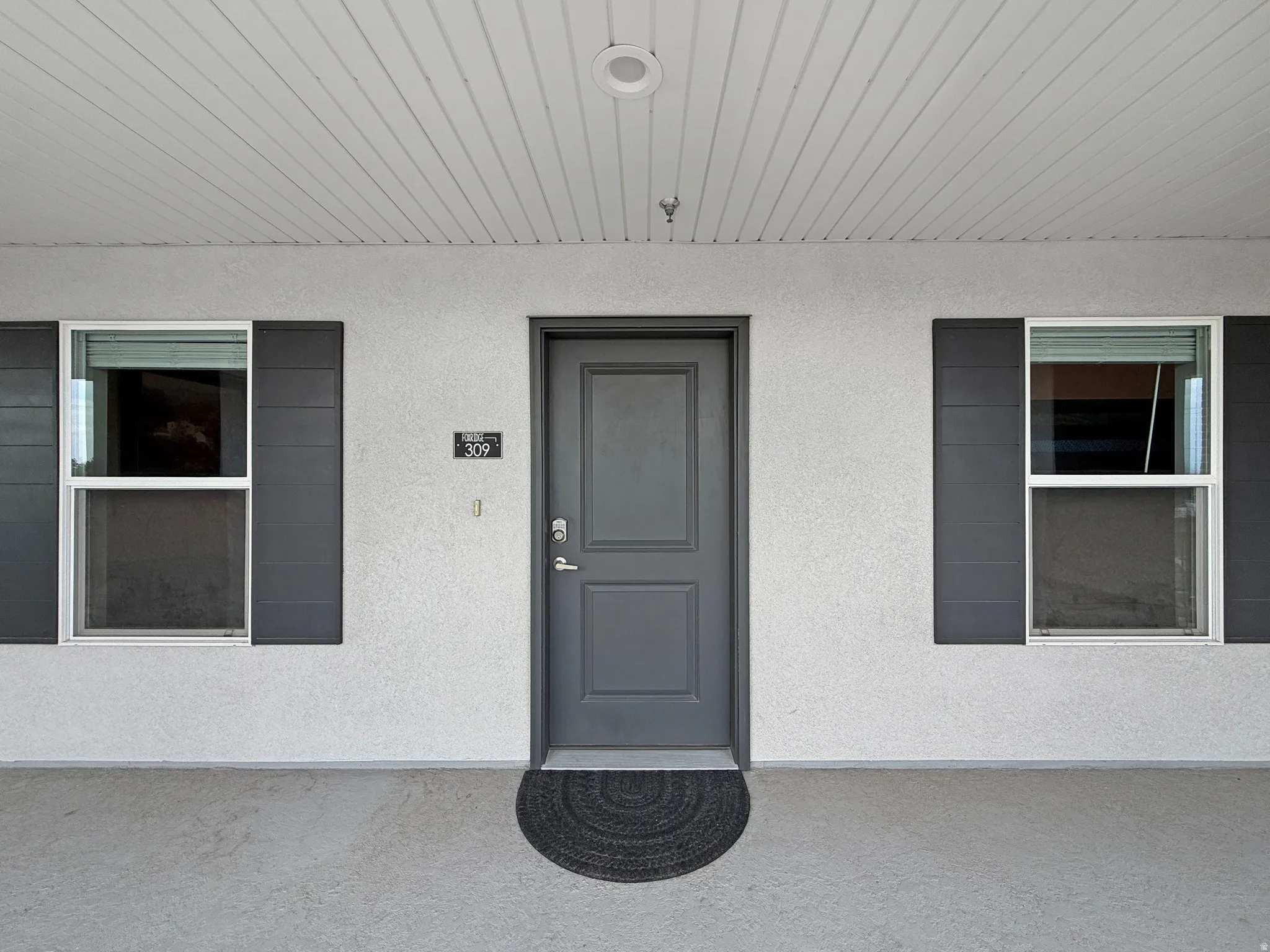 Entry door with paneled design, accompanied by two windows featuring dark shutters