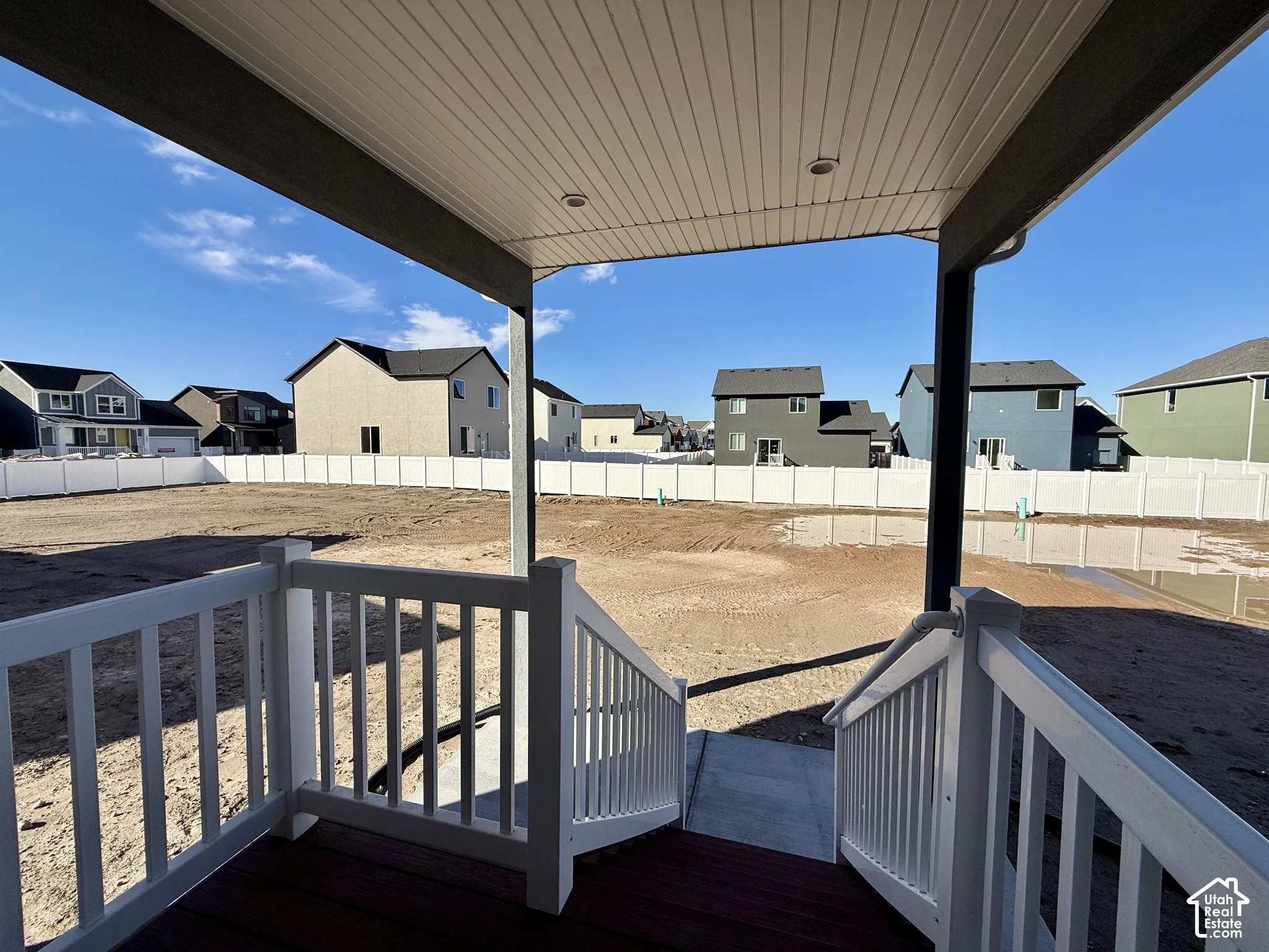 Covered porch featuring a wood-finish deck, white railing, and a vinyl privacy fence