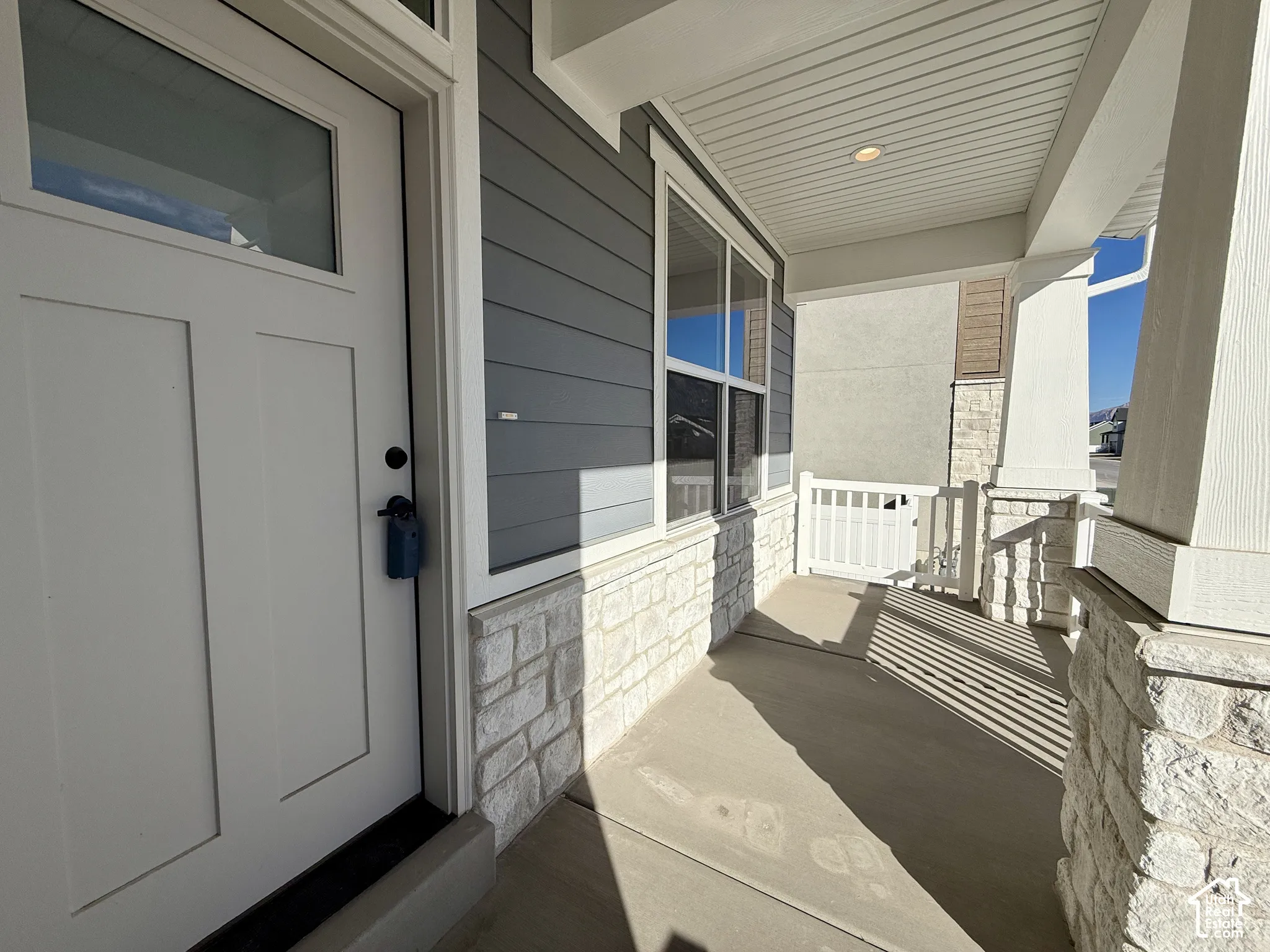 Covered entryway featuring horizontal lap siding, stone veneer base, white-framed glass paneled door, and recessed lighting