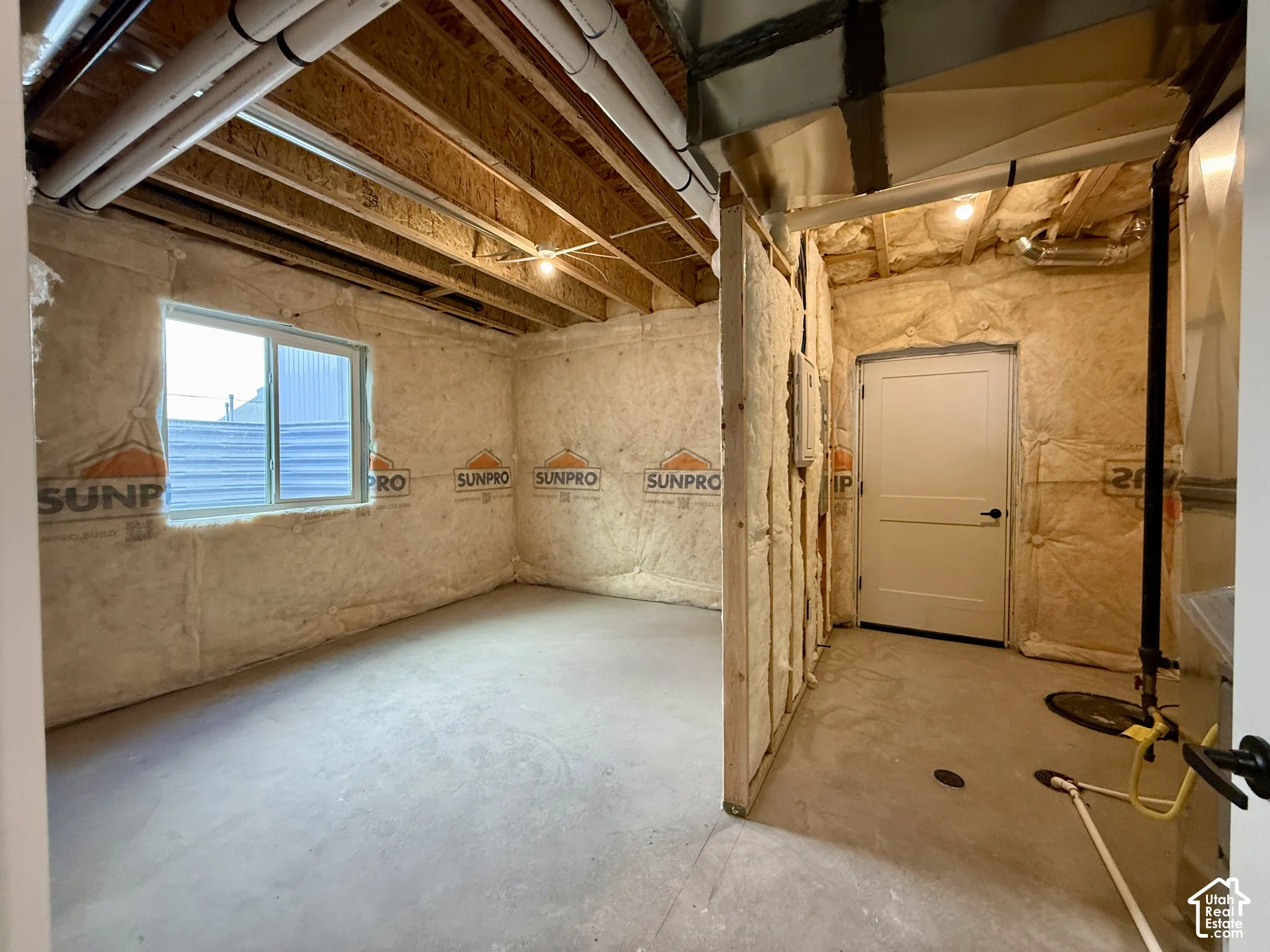 Unfinished space featuring exposed joist ceilings, fiberglass batt wall insulation, concrete flooring, a sliding window, and a paneled interior door