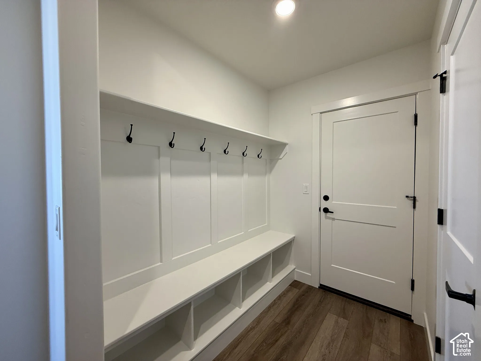 Built-in wall-to-wall storage bench with integrated shelving, overhead coat hooks, wood-finish flooring, and matte black door hardware