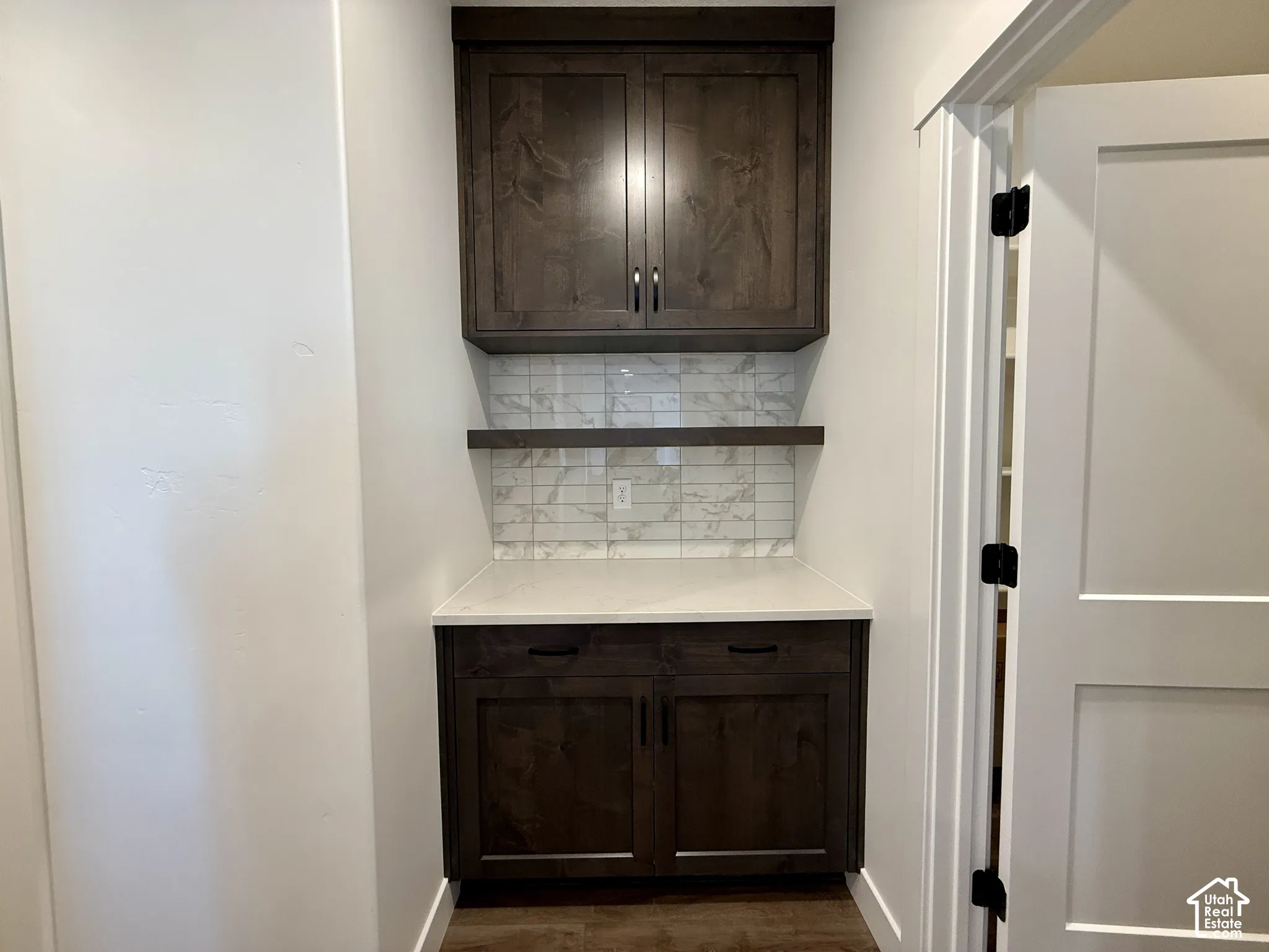 Built-in cabinetry with dark-finish wood, stone-pattern tile backsplash, solid-surface countertop, and matching floating wood shelf