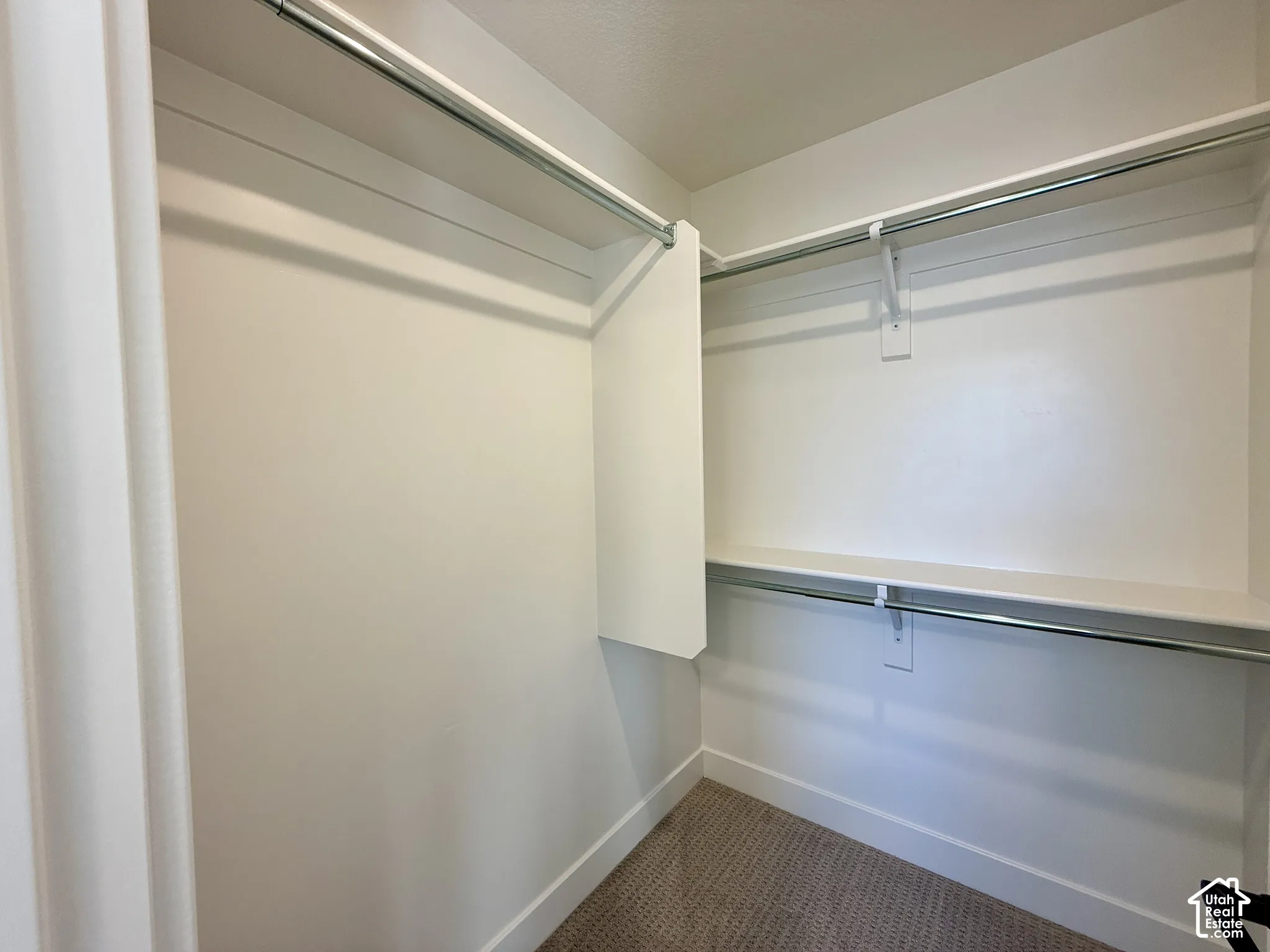 Walk-in closet featuring tiered metal garment rods, white shelving, and neutral carpeting