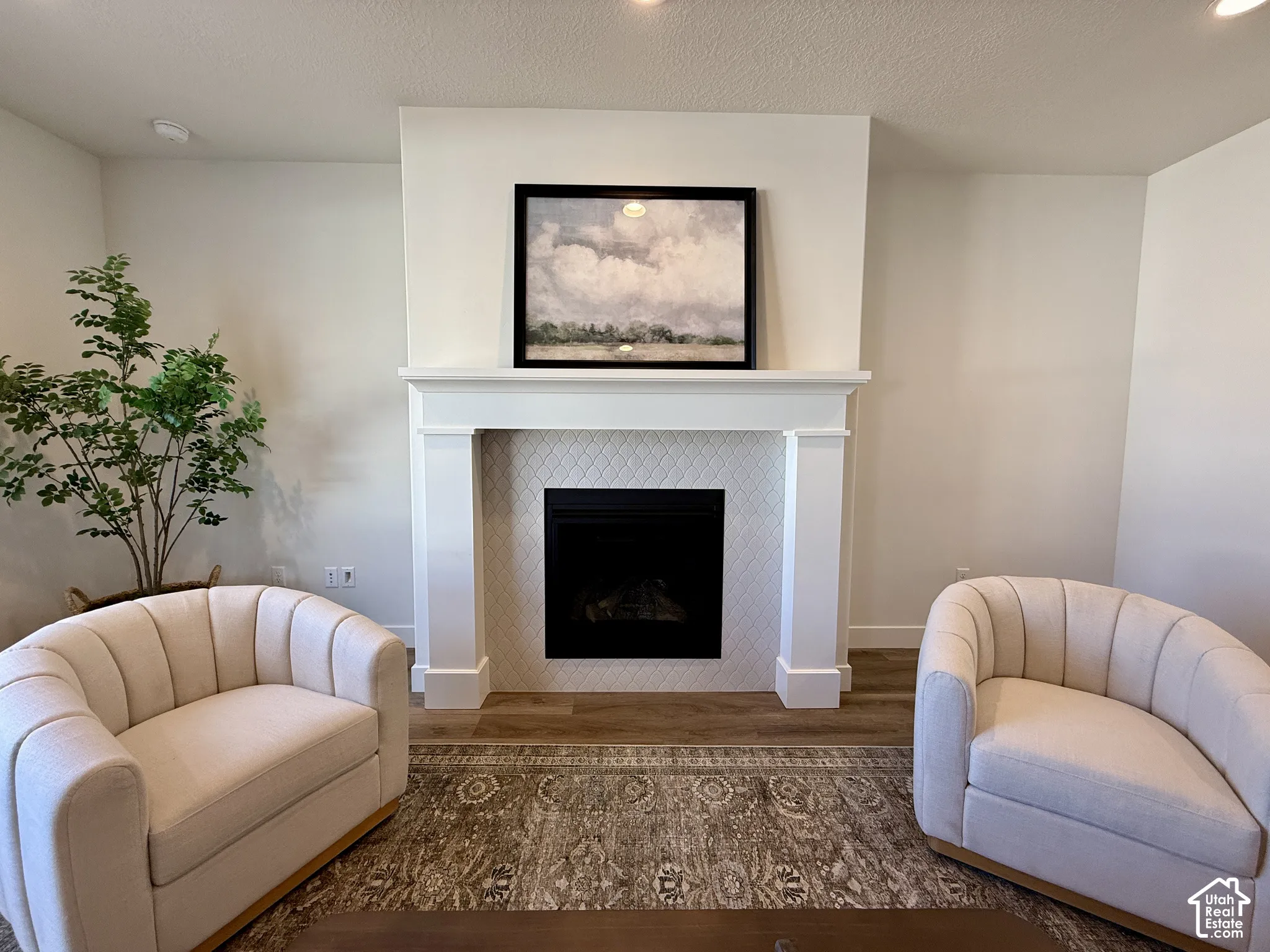 Fireplace featuring a white mantel, diamond-patterned tile surround, and wood-finish flooring