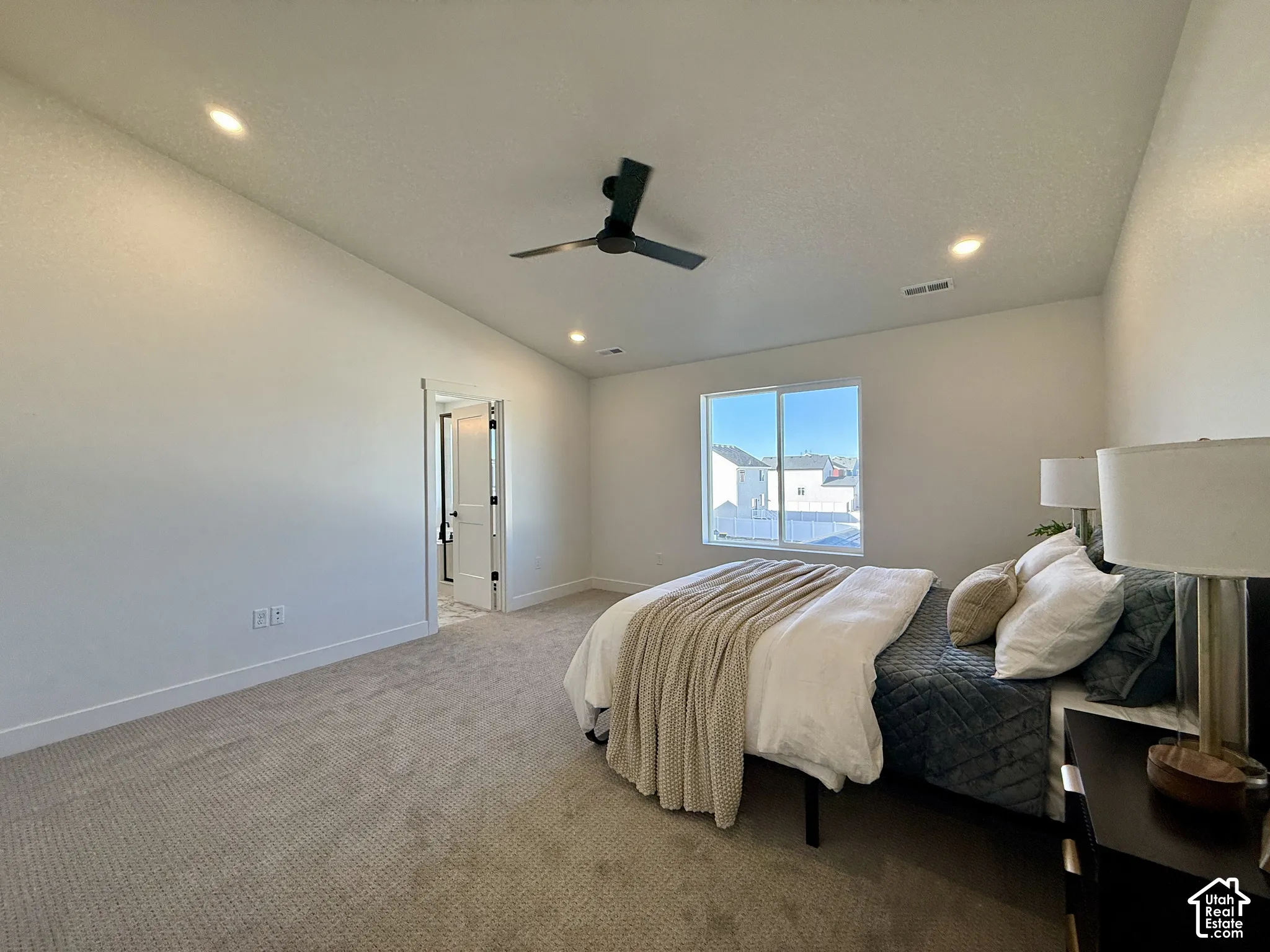 Vaulted ceiling with recessed lighting and a matte black ceiling fan, complemented by neutral carpeting and a sliding glass window