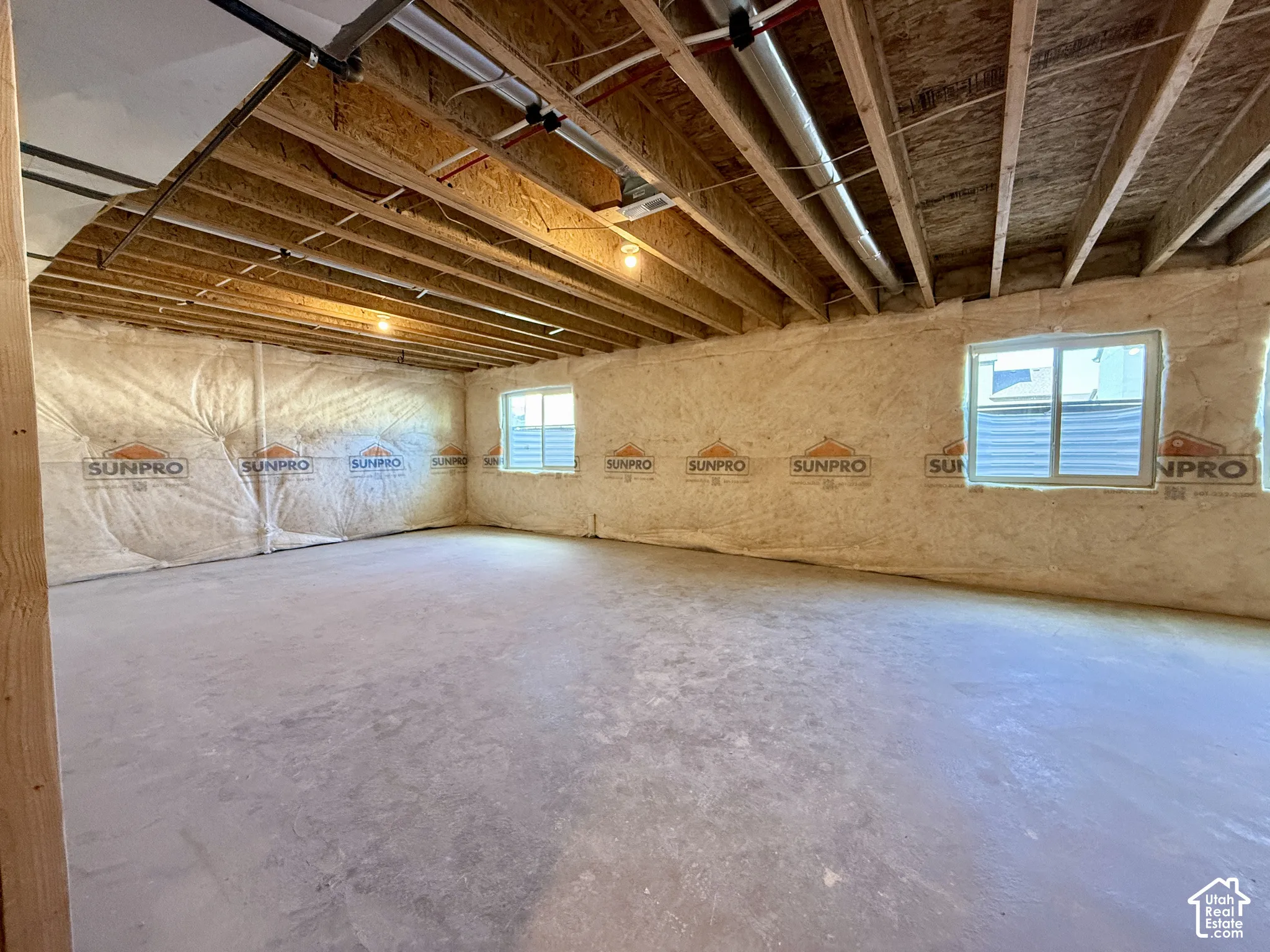 Unfinished lower level featuring concrete flooring, exposed wood-joist ceiling, and insulated perimeter walls with two egress-style windows